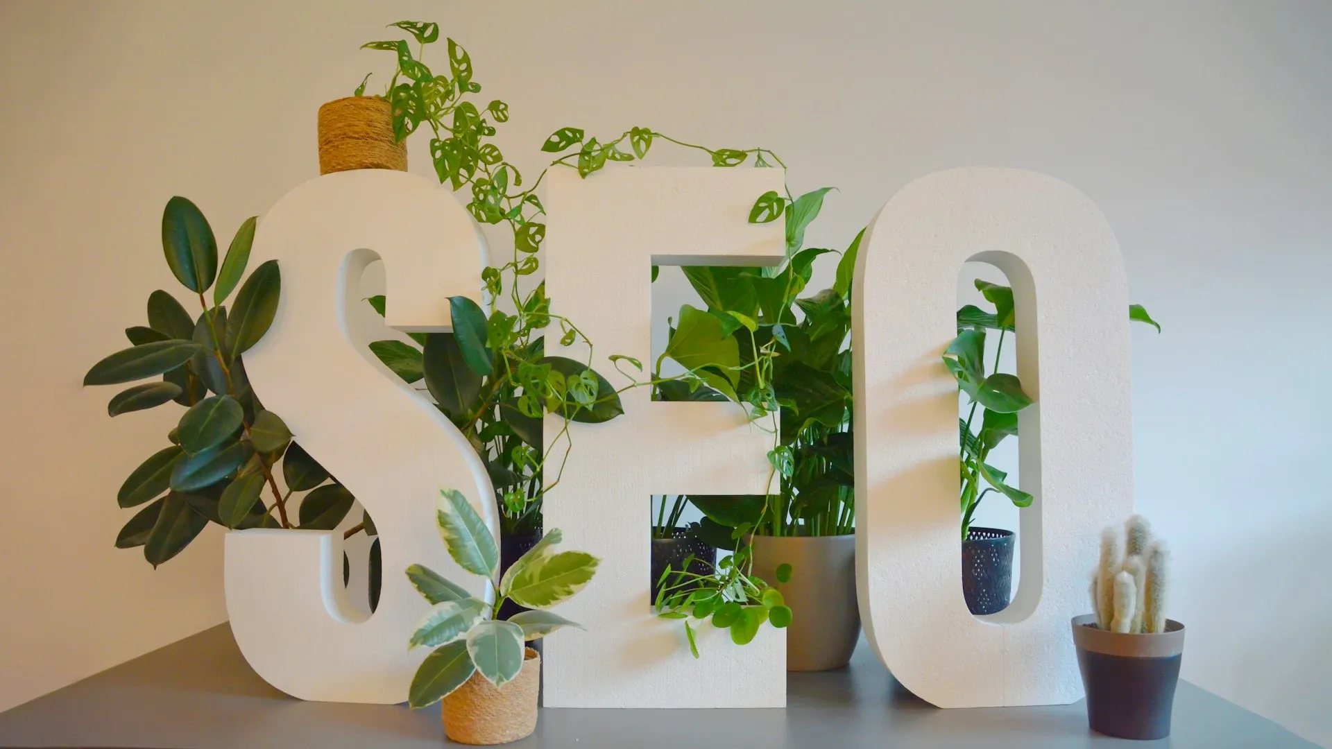 Modern desk with large 'SEO' letters covered in lush green plants in a bright office.